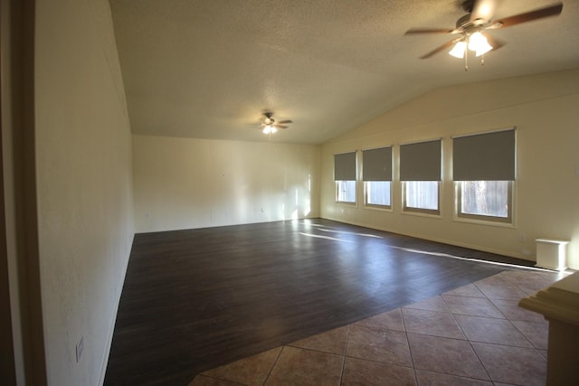 empty room featuring vaulted ceiling, a textured ceiling, dark tile patterned flooring, and ceiling fan