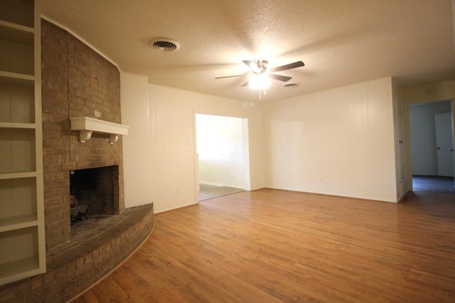 unfurnished living room featuring built in features, hardwood / wood-style flooring, ceiling fan, a brick fireplace, and a textured ceiling