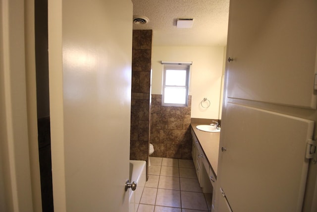 bathroom with tile walls, vanity, toilet, tile patterned floors, and a textured ceiling