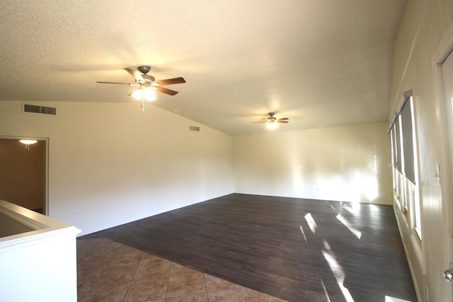 empty room featuring lofted ceiling, dark tile patterned flooring, a textured ceiling, and ceiling fan