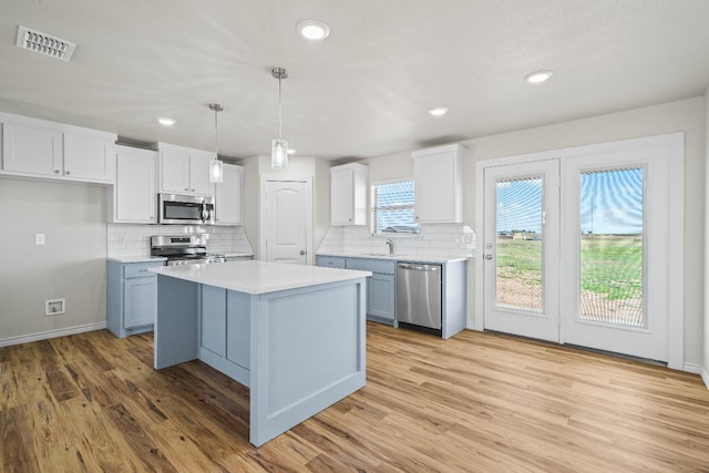 kitchen with light hardwood / wood-style flooring, appliances with stainless steel finishes, white cabinetry, hanging light fixtures, and a kitchen island