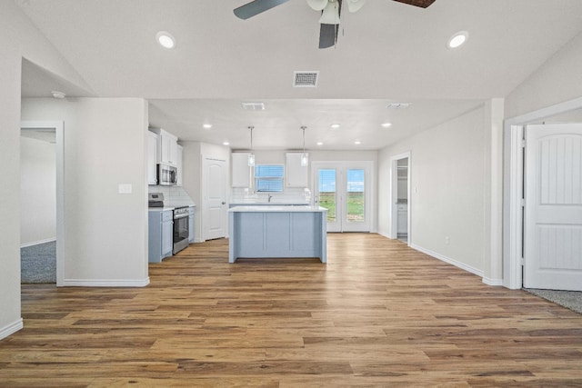 kitchen with appliances with stainless steel finishes, hanging light fixtures, white cabinets, a kitchen island, and decorative backsplash