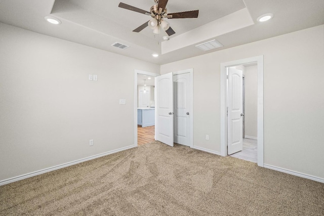 unfurnished bedroom featuring connected bathroom, a tray ceiling, and light colored carpet