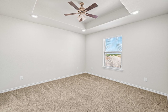 carpeted spare room featuring a raised ceiling and ceiling fan