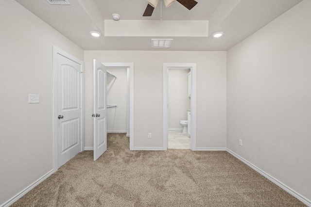 unfurnished bedroom featuring a walk in closet, light colored carpet, a tray ceiling, ensuite bath, and a closet