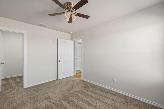 unfurnished bedroom featuring light carpet, a walk in closet, a closet, and ceiling fan