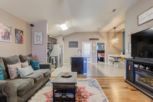 living room featuring vaulted ceiling, sink, and light hardwood / wood-style flooring