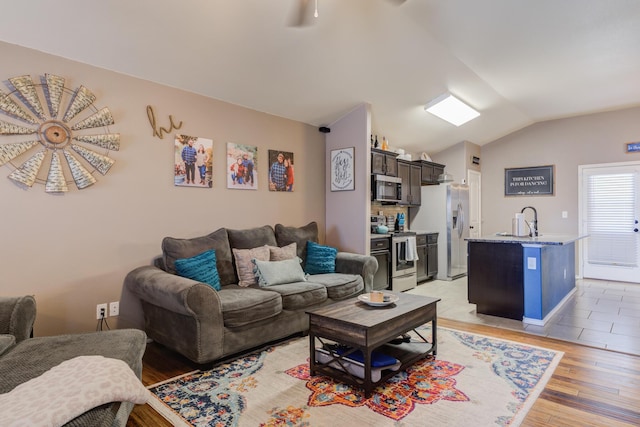 living room featuring lofted ceiling, sink, and light hardwood / wood-style floors