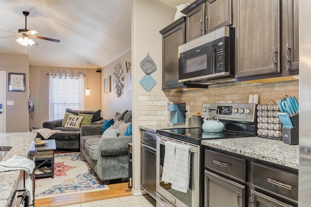 kitchen with lofted ceiling, dark brown cabinets, appliances with stainless steel finishes, light stone countertops, and backsplash