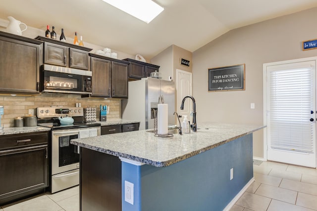 kitchen featuring lofted ceiling, light tile patterned floors, dark brown cabinetry, stainless steel appliances, and a center island with sink