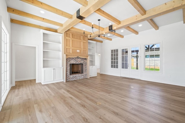 unfurnished living room with an inviting chandelier, light wood-type flooring, a brick fireplace, beam ceiling, and french doors