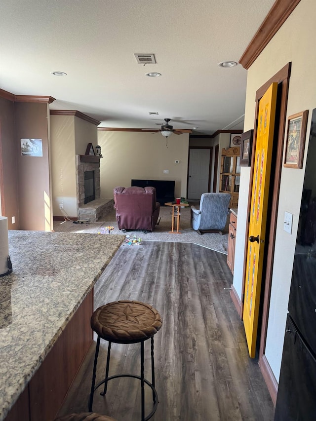 interior space featuring crown molding, a stone fireplace, dark hardwood / wood-style floors, and ceiling fan