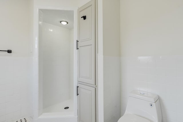 bathroom featuring tiled shower, toilet, and tile walls