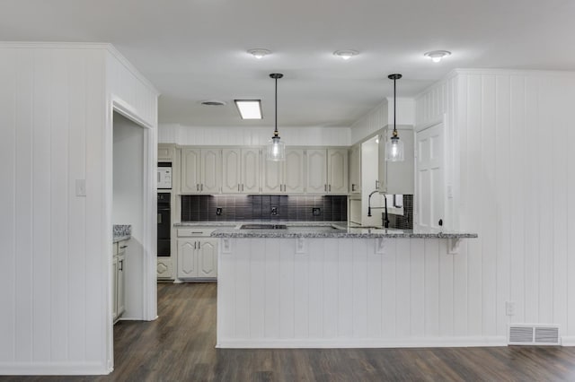 kitchen with decorative light fixtures, dark wood-type flooring, kitchen peninsula, and stone counters