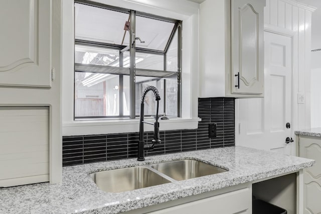 kitchen featuring white cabinetry, light stone countertops, sink, and backsplash