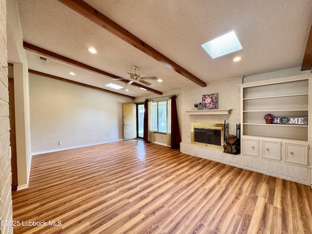 5508 94th St, Lubbock, TX 79424 - unfurnished living room with a textured ceiling, a skylight, light wood-type flooring, a brick fireplace, and beam ceiling