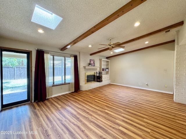 5508 94th St, Lubbock, TX 79424 - unfurnished living room with a textured ceiling, beam ceiling, a glass covered fireplace, light wood-style flooring, and a skylight