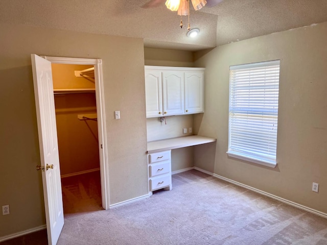 unfurnished office with ceiling fan, built in desk, light colored carpet, and a textured ceiling