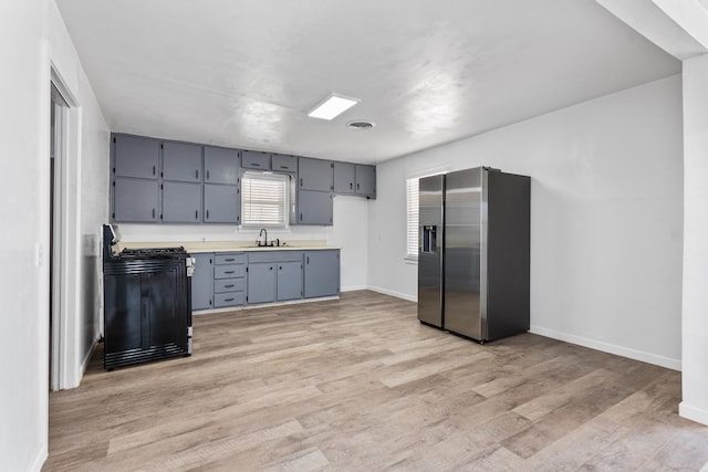 kitchen with sink, gray cabinetry, stove, light hardwood / wood-style floors, and stainless steel fridge with ice dispenser