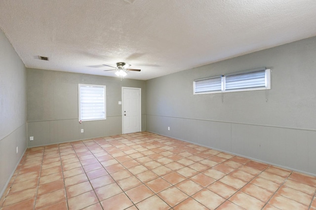 empty room with ceiling fan, light tile patterned floors, and a textured ceiling