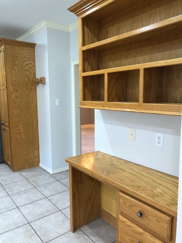 unfurnished office with crown molding, built in desk, and light tile patterned floors