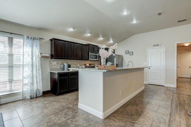 9207 Trenton Ave, Lubbock, TX 79424 - kitchen featuring appliances with stainless steel finishes, lofted ceiling, backsplash, an island with sink, and light stone counters