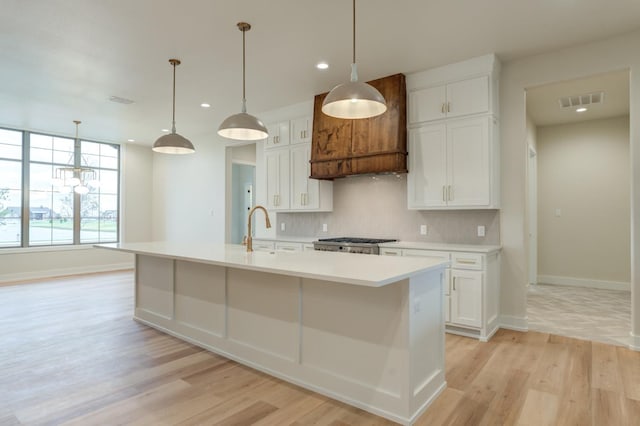 kitchen featuring a center island with sink, white cabinets, backsplash, and decorative light fixtures