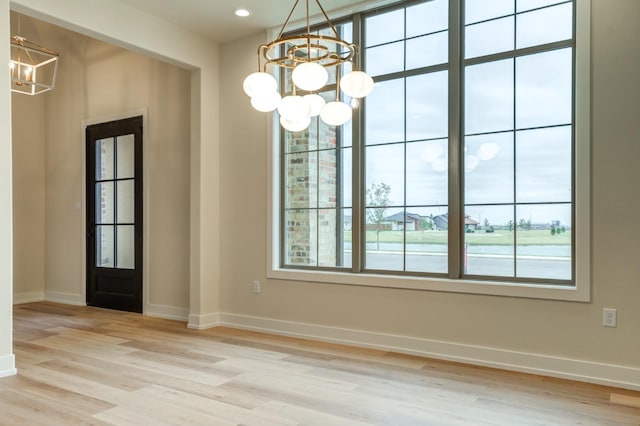 unfurnished dining area featuring an inviting chandelier, light hardwood / wood-style floors, and a wealth of natural light