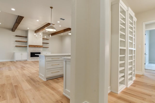 kitchen featuring white cabinetry, light wood-type flooring, beam ceiling, and decorative light fixtures