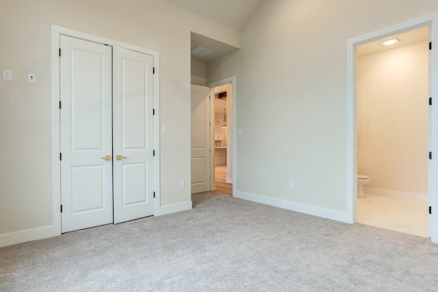 unfurnished bedroom featuring light colored carpet, ensuite bath, and a closet