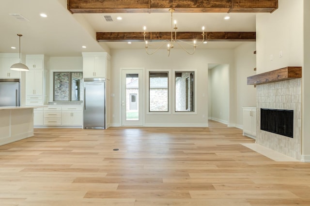 unfurnished living room with a tiled fireplace, light hardwood / wood-style flooring, beamed ceiling, and an inviting chandelier