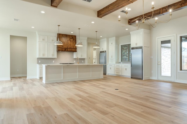 kitchen featuring decorative light fixtures, white cabinetry, stainless steel fridge, built in refrigerator, and a large island with sink