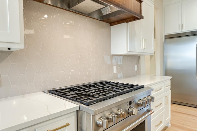 kitchen with wall chimney range hood, backsplash, high quality appliances, light stone countertops, and white cabinets