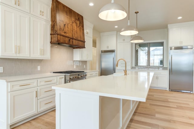 kitchen with high end appliances, pendant lighting, a kitchen island with sink, and white cabinetry