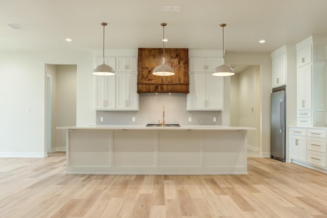 kitchen featuring white cabinets, a kitchen island with sink, high end fridge, and decorative light fixtures