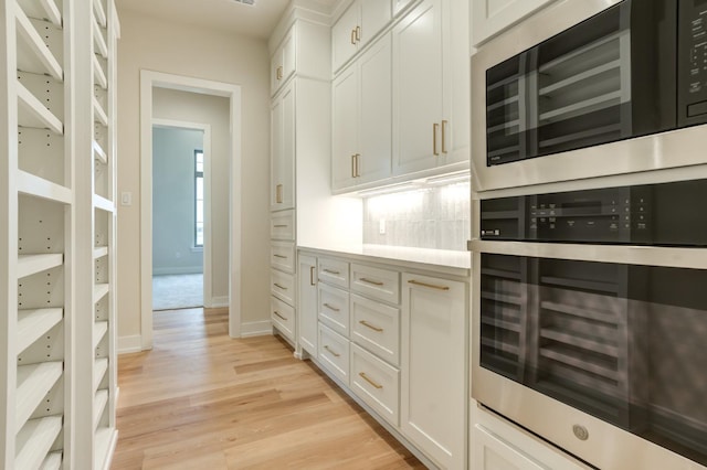 interior space featuring tasteful backsplash, appliances with stainless steel finishes, white cabinets, and light hardwood / wood-style floors