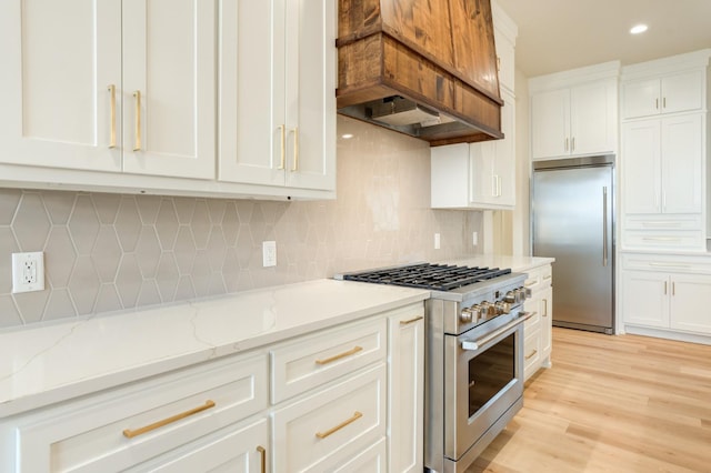 kitchen featuring high end appliances, white cabinetry, light stone counters, and backsplash