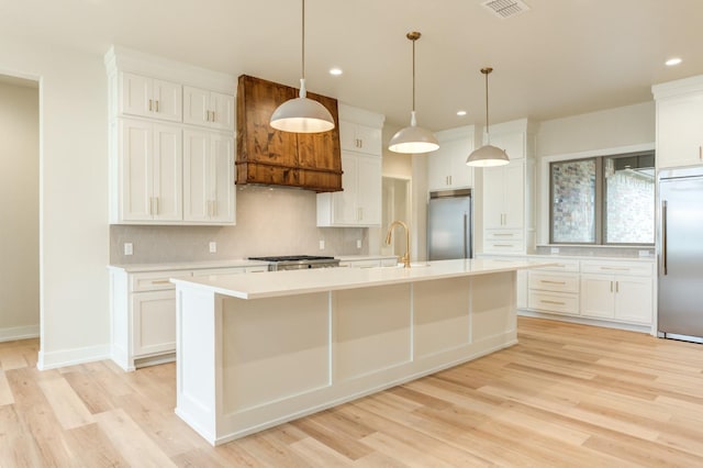 kitchen with stainless steel built in refrigerator, a kitchen island with sink, and white cabinets