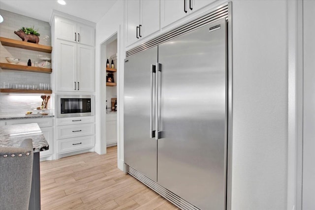 kitchen featuring white cabinetry, tasteful backsplash, built in appliances, and light hardwood / wood-style flooring