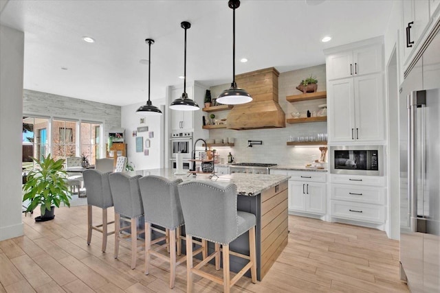 kitchen with white cabinetry, light stone counters, decorative light fixtures, black microwave, and a kitchen island with sink