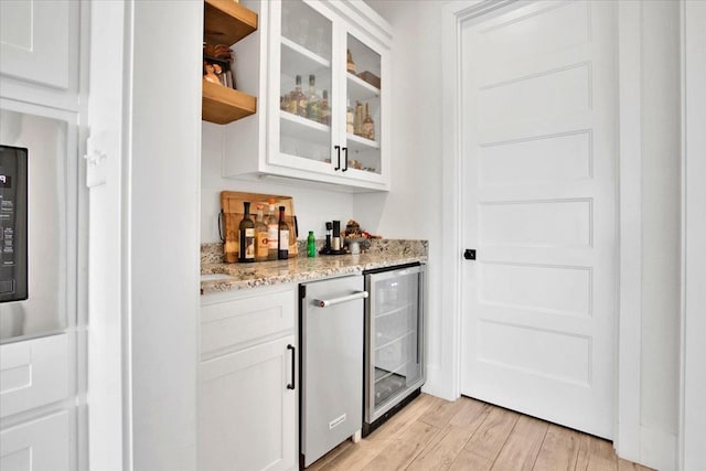 bar featuring white cabinetry, light stone counters, light hardwood / wood-style floors, and beverage cooler