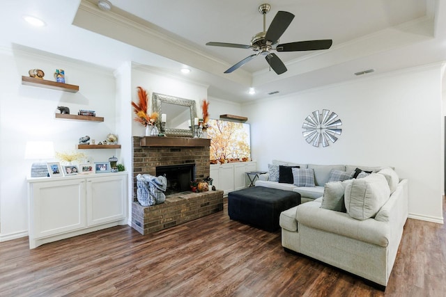 living room featuring ceiling fan, dark hardwood / wood-style floors, a tray ceiling, a fireplace, and ornamental molding