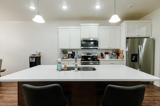 kitchen with decorative light fixtures, ornamental molding, an island with sink, stainless steel appliances, and white cabinets