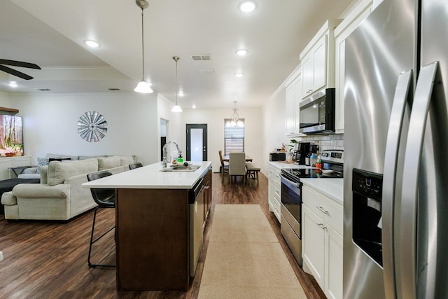 kitchen featuring pendant lighting, sink, appliances with stainless steel finishes, white cabinetry, and a center island with sink