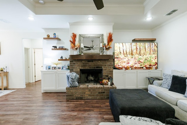 living room featuring ceiling fan, dark hardwood / wood-style floors, ornamental molding, a brick fireplace, and a raised ceiling