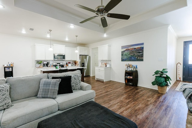 living room featuring crown molding, dark wood-type flooring, a raised ceiling, and ceiling fan