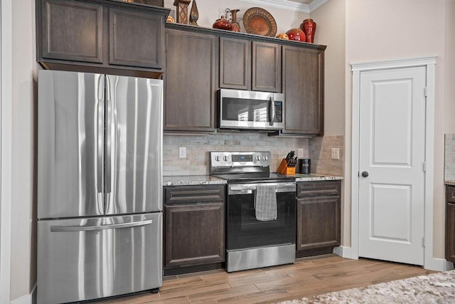 kitchen with decorative backsplash, light stone counters, stainless steel appliances, dark brown cabinets, and light wood-type flooring