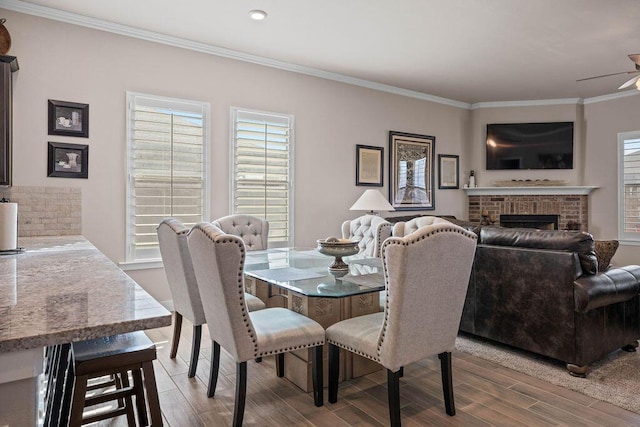 dining area featuring crown molding, ceiling fan, and a brick fireplace