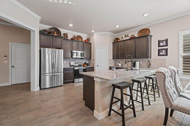 kitchen with a kitchen bar, dark brown cabinetry, stainless steel appliances, light stone countertops, and light hardwood / wood-style flooring