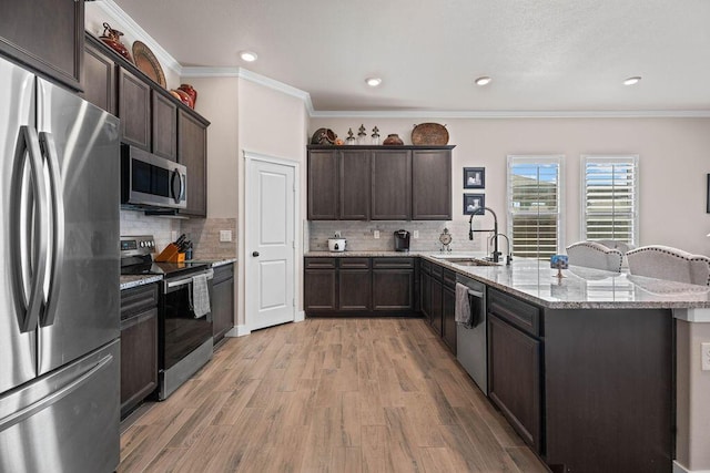 kitchen with sink, stainless steel appliances, light stone counters, ornamental molding, and light wood-type flooring